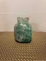 Front view of small carved jade vase with textured pattern and slight top rim roughness.