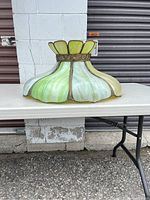 Side view of stained glass lamp shade with shades of green and white with metal floral detail.
