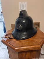 Front and side view of black leather fireman’s helmet showing worn badge area and ridge detail.