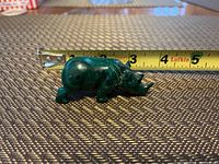 Side view of malachite rhinoceros figurine next to tape measure showing length about 2.5 inches