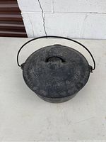 Top angled view of cast iron Dutch oven with lid and handle, showing embossed branding and text on lid.