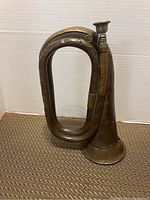 Full side view of the brass military bugle showing its coiled shape and aged patina