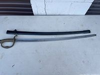 Full view of sword unsheathed on table showing curved blade and black metal scabbard