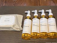 Four bottles of Manyo Pure Cleansing Oil arranged horizontally with one pack of Re:NK Professional Cleansing Oil Tissue on the left, all sealed.