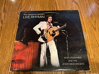 Front cover of the vinyl record showing Paul Simon playing guitar in white suit with text details.