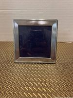 Front view of square sterling silver picture frame showing decorative border and empty photo slot.