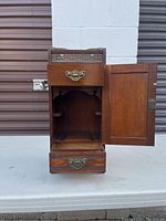 Front view of open pipe stand door showing interior compartment with two curved pipe holders and upper drawer.