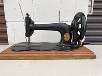 Side view of the black antique Singer sewing machine with gold detailing on a wooden base.