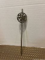 Front view of a sterling silver Japanese hair pin with a circular top featuring floral and geometric cutouts and a long, slender pin.