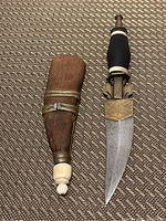 Tuareg tribal dagger next to its decorated wooden and brass sheath, showing the blade and detailed handle with ivory-like rings.