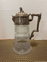Full view of the Victorian claret jug showing cut glass body and ornate silver plated top and handle with lion finial lid.