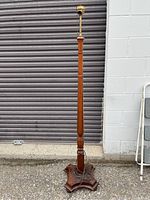 Full height photo of the wooden floor lamp standing upright showing the tall turned wooden column and the brass-colored socket at the top.
