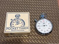 Photo showing a Zonex pocket timer stopwatch next to its original box. The stopwatch is a round chrome case with a white dial and black and red numerals. The box is white with blue illustration and text 'POCKET TIMER SWISS PRECISION'.
