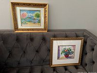 Full view of two framed artworks atop a grey tufted sofa, showing size and framing style