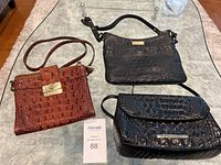 Three Brahmin croc-embossed leather purses, two black and one brown, displayed on a table