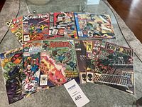 Photo showing 12 comic books laid out on a table with visible covers including Fantastic Four, X-Factor, Avengers, Spawn, WildC.A.T.s, and Ragman