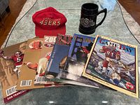 Lot including red SF 49ers cap, black ceramic stein with 49ers emblem, and seven GameDay sports magazines.