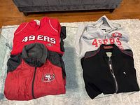 All four San Francisco 49ers jackets folded on a glass table, showing front logos and colors.