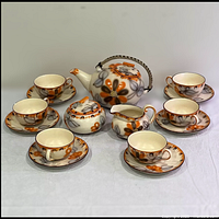 Full 17 piece set displayed on table including teapot, sugar bowl, creamer, 6 cups, and 6 saucers with floral orange, brown and gray design.