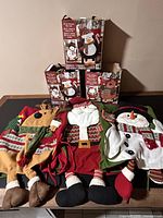 Photo showing six Christmas chair covers featuring Santa, two snowmen, two penguins, and a moose, with packaging visible behind them.