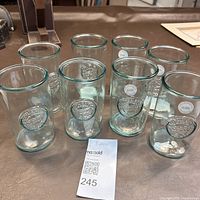 Front view of all 8 recycled glass drinking glasses arranged in two rows, showing embossed logos and overall shape.