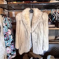 Front view of vintage cream/blue fox fur jacket hanging, showing length and shape, fluffy fur texture visible.