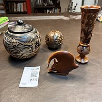 Four carved wood items including a black and tan carved jar, spherical wood ball, carved animal figure, and carved wood vase on a table