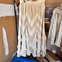 Front view of vintage beige cotton skirt with chevron lace details, hanging on rack