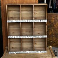Full view of the wooden cubby shelf showing nine compartments and three horizontal tin strips with numbered tags 1 to 9.