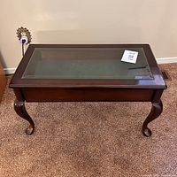Top angled view of a dark wood veneer display table with a large inset glass panel and an open drawer showing green velveteen lining.