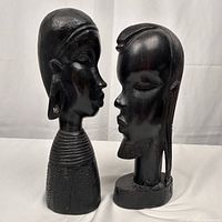 Front and side views of two handcarved ebony wood Maasai head sculptures, showing detailed facial features, traditional jewelry, and textured neck rings.