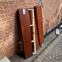 Three dark wood floating shelves leaning against a brick wall, with visible mounting structure on the back of one shelf