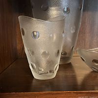 View of medium-sized frosted glass vase with raised polka dots on dark wooden shelf.
