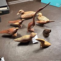 Lot of nine hand carved wood bird sculptures of various sizes, wood types, and styles arranged on a brown surface.