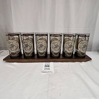 Front view of six glasses arranged on a wooden stand showing detailed Old World compass design on each glass.