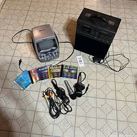 Memorex karaoke machine with built-in TV screen, Genexxa karaoke machine, microphones, cords and karaoke music CDs arranged on floor with tiled pattern.