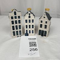 Front view of three white ceramic miniature houses with detailed windows and doors, blue and black paint detailing, and yellow chimneys.