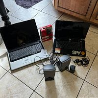 Photo showing Dell Inspiron 1545 laptop, Dell Inspiron 1750 laptop, two Harman Kardon speakers, and boxed LifeCam VX-2000 webcam along with cables and adapter on tiled floor.