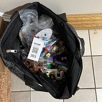 Overhead view of black duffel bag filled with assorted LEGO pieces in plastic bags inside.