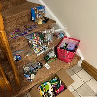 Full lot overview showing assorted Lego bags, partial builds, instruction booklets and a storage bin on stair steps and floor.