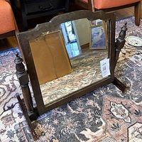 Front angled view of vintage wooden tabletop swinging mirror placed on patterned rug, showing reflective mirror surface and wooden detail.