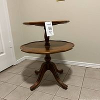 Side-angle view showing two-tier wooden table with scalloped edges and central turned pedestal with four curved legs.