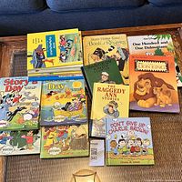 Full view of all 16 vintage children's books laid out on table including Story a Day sets, Deans Mother Goose, Raggedy Ann, Disney Dalmatians, Lion King, and Charlie Brown books.