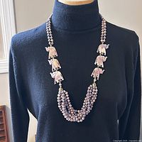 Full view of vintage multi-strand purple beaded necklace with carved elephant pendants worn on black turtleneck.