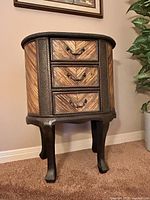 Front and side perspective of wood accent table showing rattan-covered drawers and dark carved wood legs.