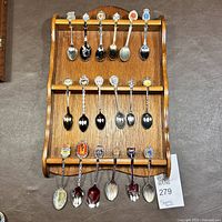 Full view of wooden rack holding 18 assorted collectible spoons arranged in three rows, showing colorful spoon handles.