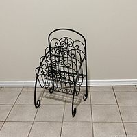 View of mid-century wrought iron magazine rack showing front and decorative scroll pattern.