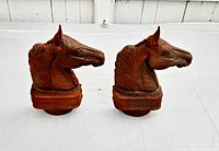 Two vintage cast iron half horseheads upright and side by side on a white surface, showing full frontal and right side profiles, with a rusty brown patina.