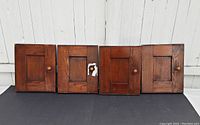 Four small vintage oak doors or panels arranged side-by-side showing front faces with different handles and overall condition