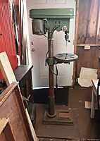 Front view of full drill press showing structure, base, column, work table and drill head assembly in an industrial setting.